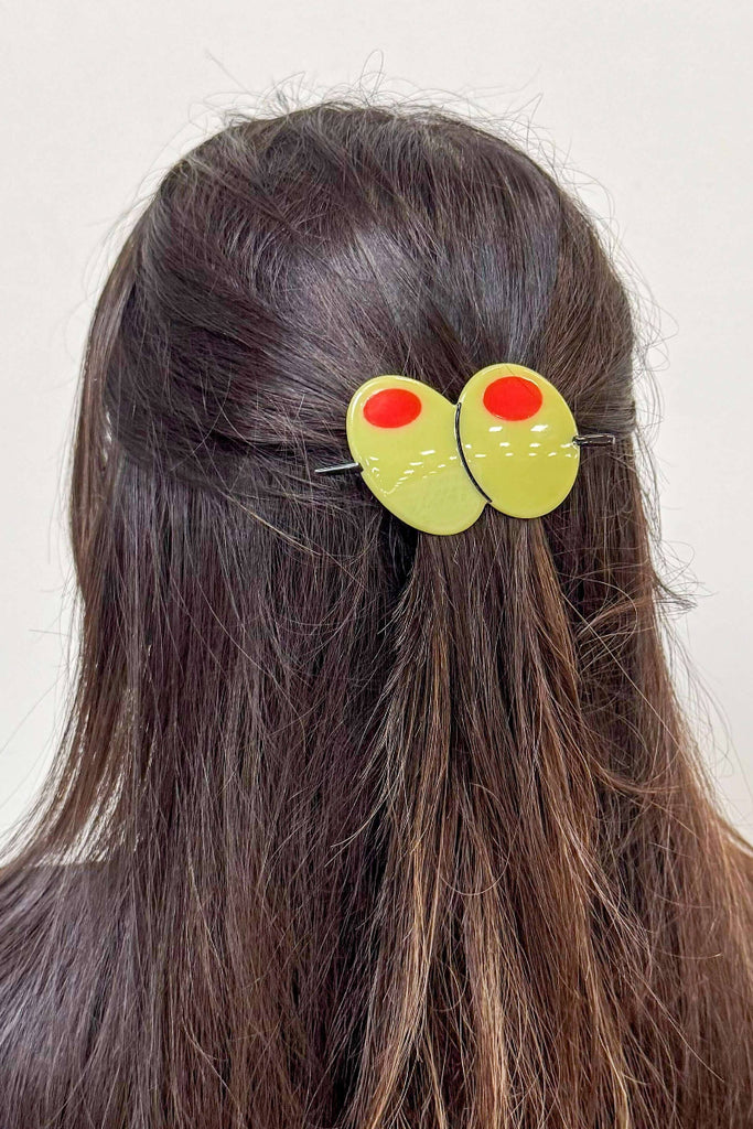 Hair clip with martini olives on a person's hair against a white background