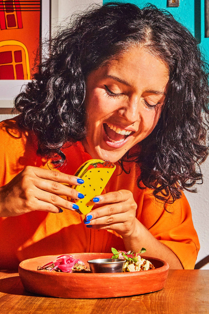 Woman in an orange shirt holding a colorful taco with a vibrant background