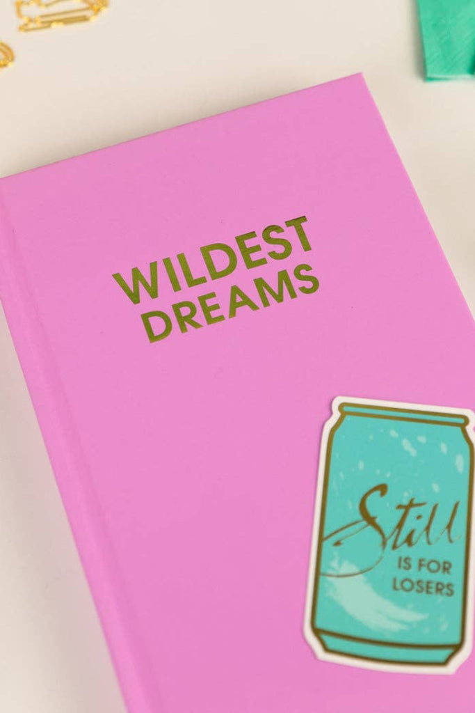 Pink notebook with 'Wildest Dreams' text and a can sticker on a light background
