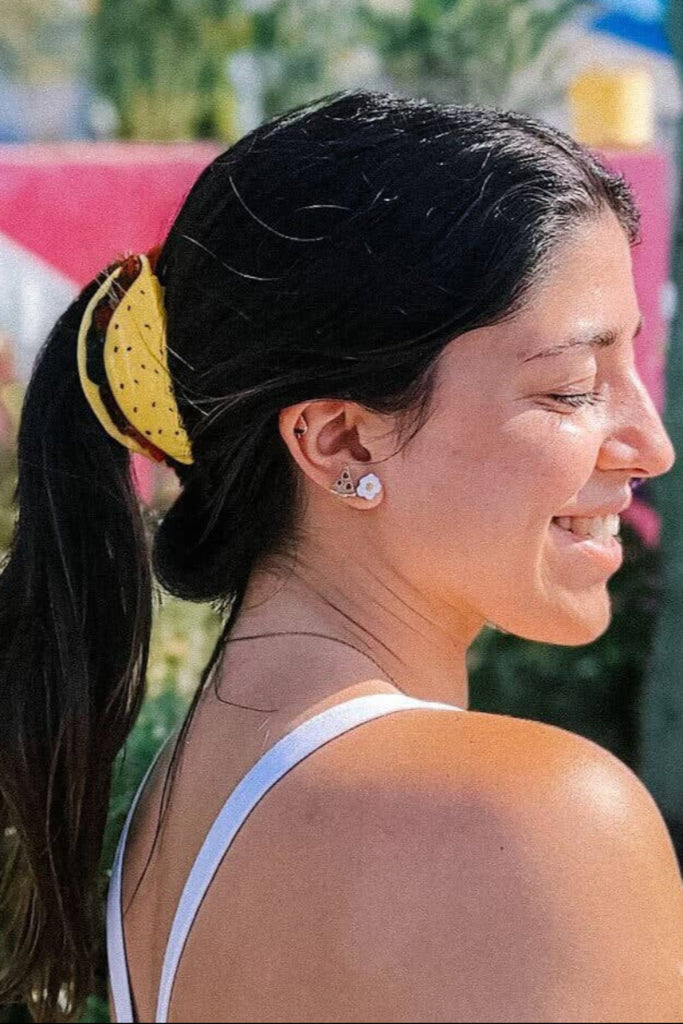 Woman with a yellow  taco hair tie in her hair, standing outdoors with greenery in the background