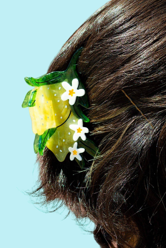 Hair clip with yellow flowers and green leaves in a person's hair against a blue background