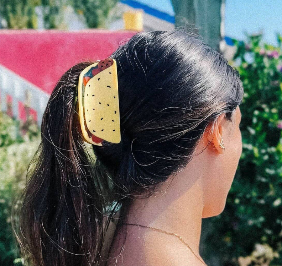 Person with a yellow tacoo shell hair clip in their hair against a blurred outdoor background