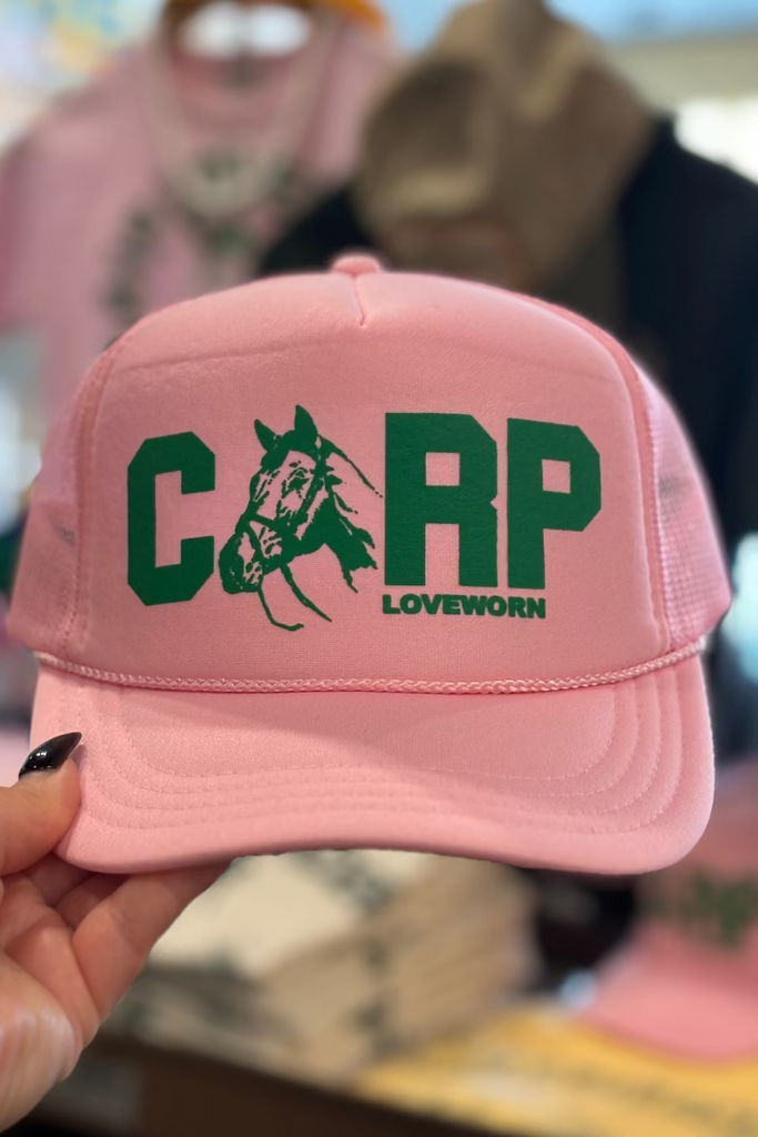 Pink cap with green text and logo held by a hand, blurred background