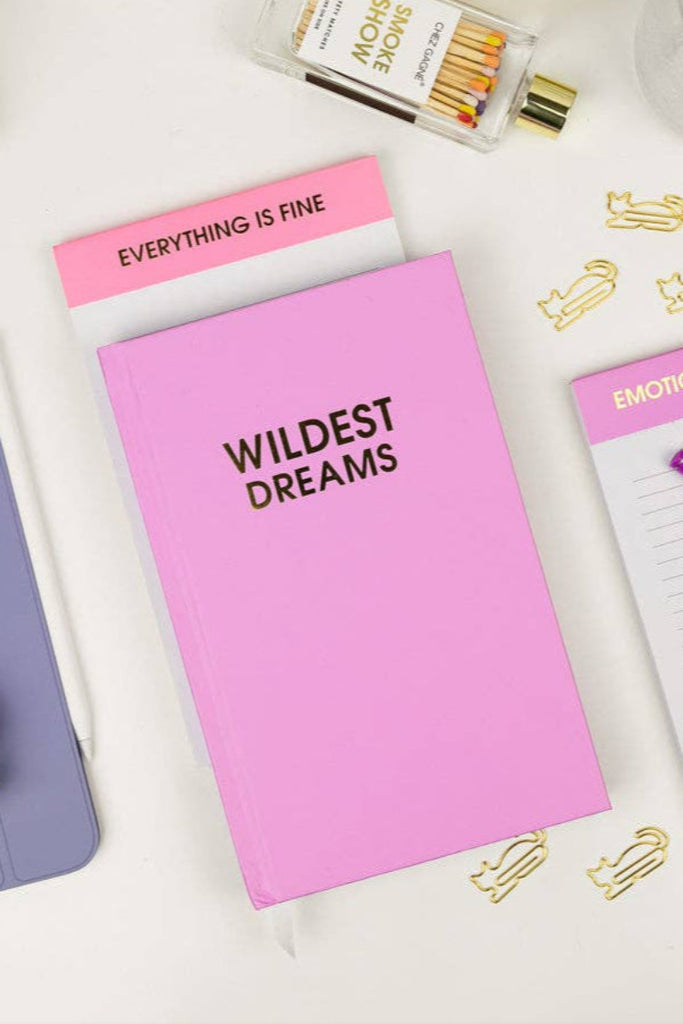 Pink notebook with 'Wildest Dreams' text, purple notebook, and various stationery items on a white surface.