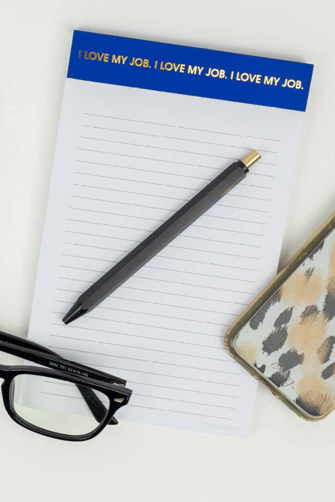 Notepad with 'I LOVE MY JOB.' text, pen, glasses, and phone on a desk.