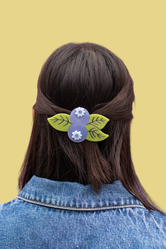 Person with a floral hair clip in their dark hair against a purple background