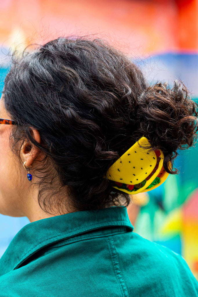 Person wearing sunglasses and a yellow taco shaped hair accessory with colorful background