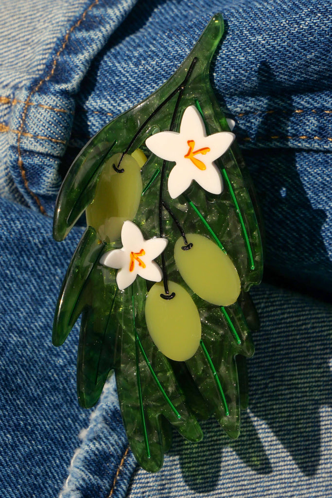 olive branch hair clip with green leaves and white flowers on a denim background