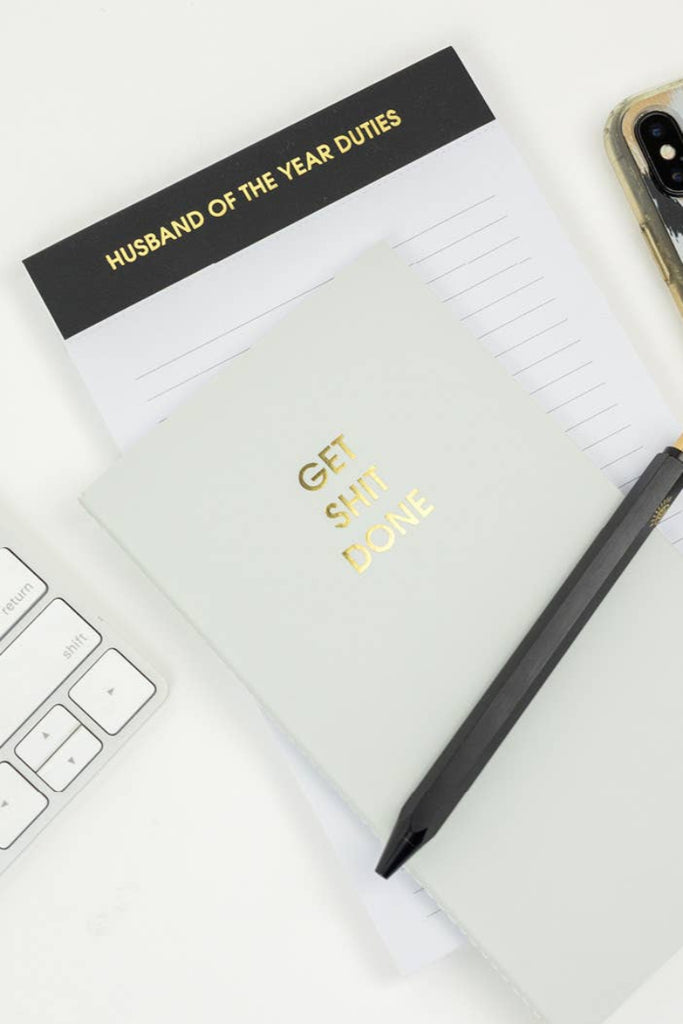Notebook titled 'Husband of the Year Duties' with a pen and phone on a desk.