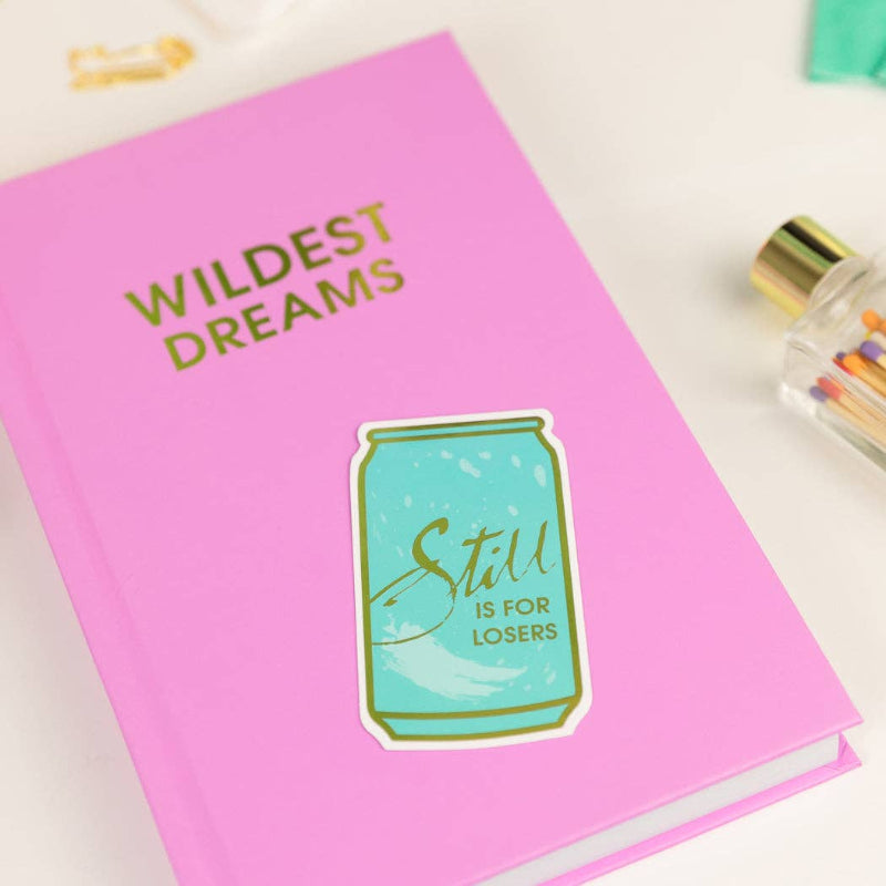 Pink notebook with 'Wildest Dreams' text and a can sticker on a white background