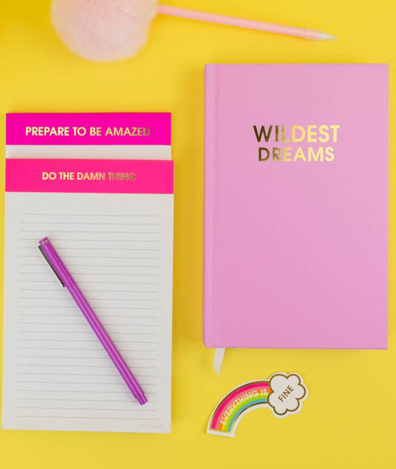 Two notebooks with motivational text on a yellow background, accompanied by a pen and decorative items. wildest dreams notebook